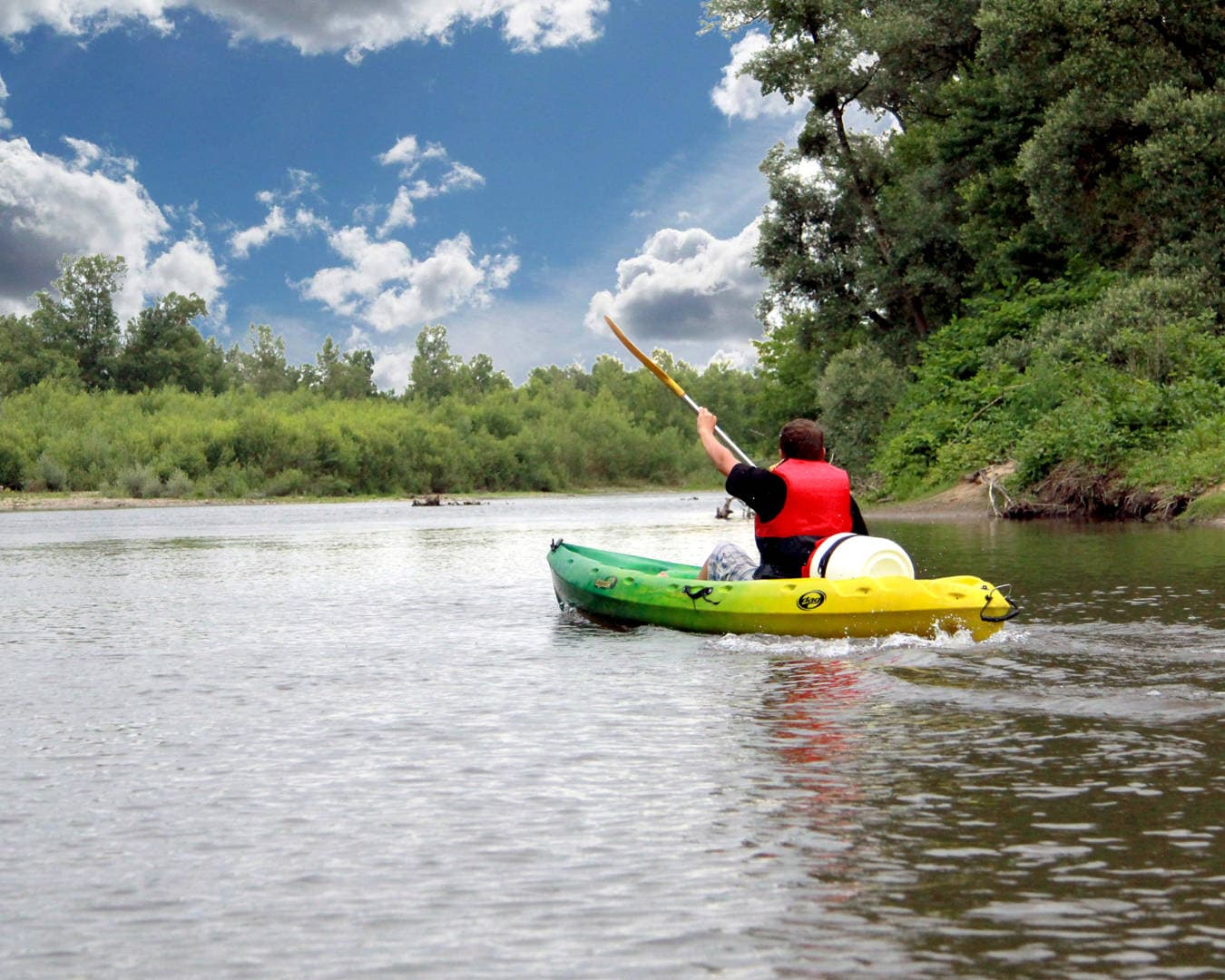 Couple pagayant en canoë sur une rivière calme et verdoyante